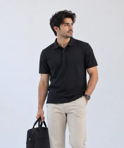 A man in a black polo shirt and stone chinos, carrying a laptop bag.