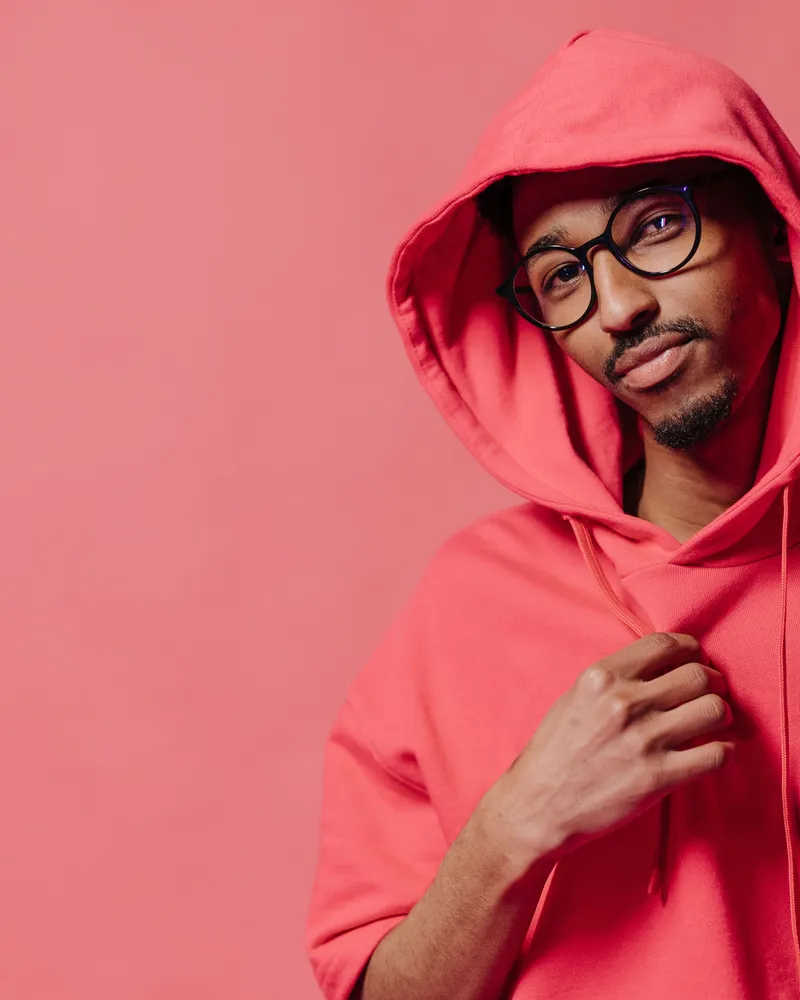 A model in a bright coral pullover hoodie against a matching studio backdrop.